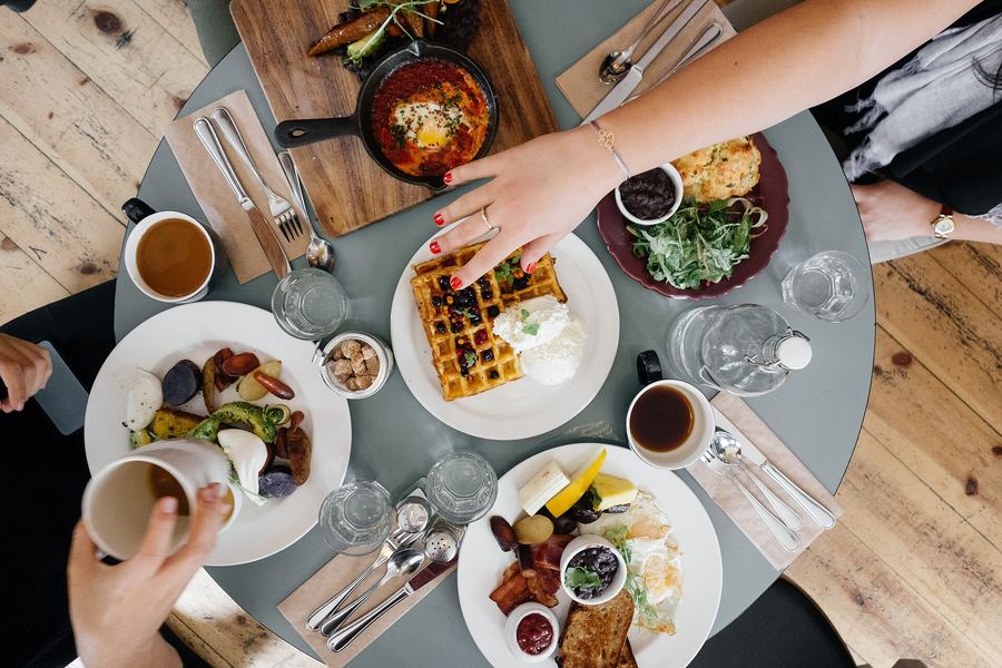 Friends reaching across a round table covered in brunch plates and coffee