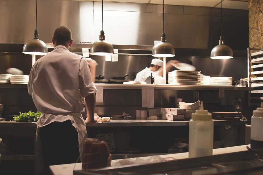A chef at the pass of an open kitchen under warm pendant lamps