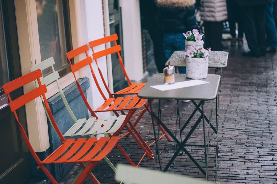 Red folding chairs and a small table outside a café on a brick street